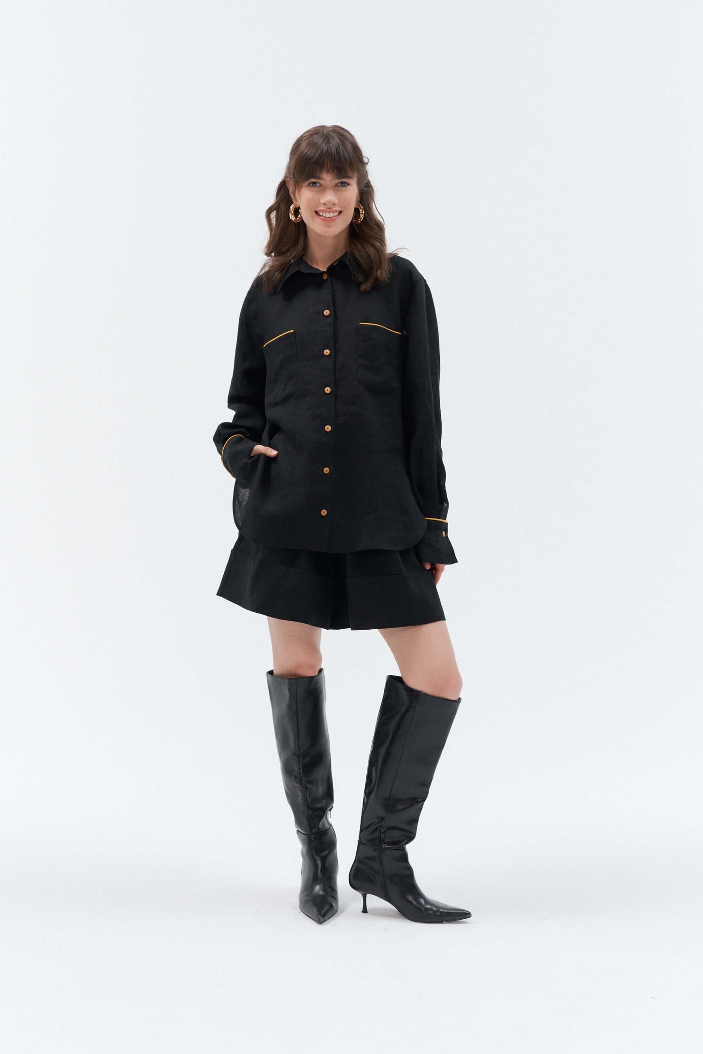 Front view of woman wearing black wide-leg linen shorts Bonita paired with the Brillante long-sleeve oversized linen shirt with yellow accents, styled with high-heeled boots.