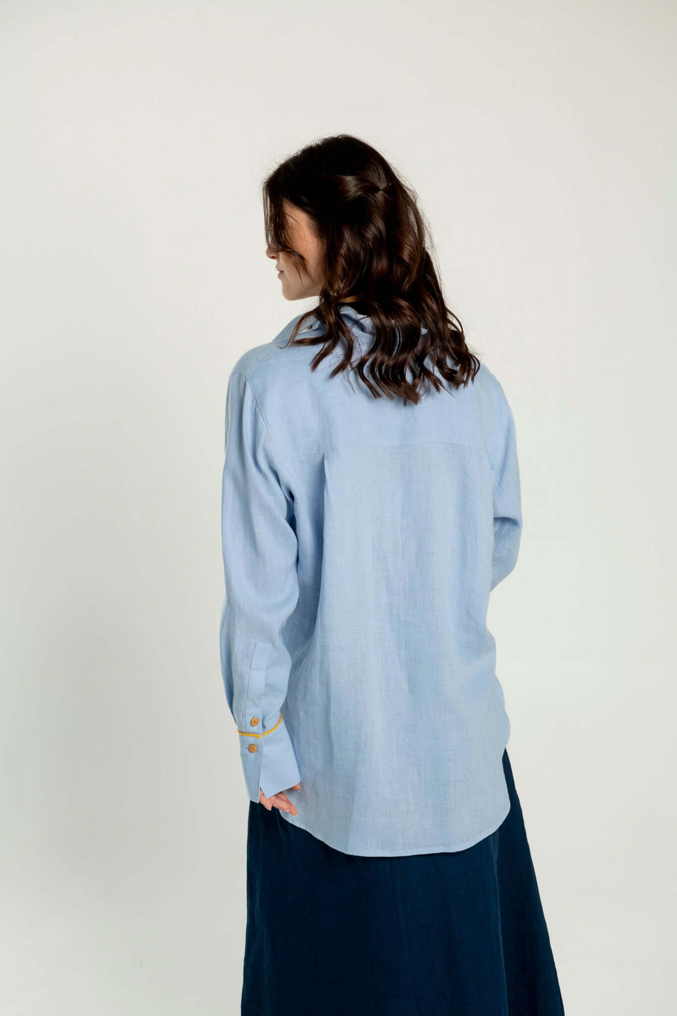 Back view of a model wearing an Oversized linen shirt with yellow details Brillante in light blue fabric.