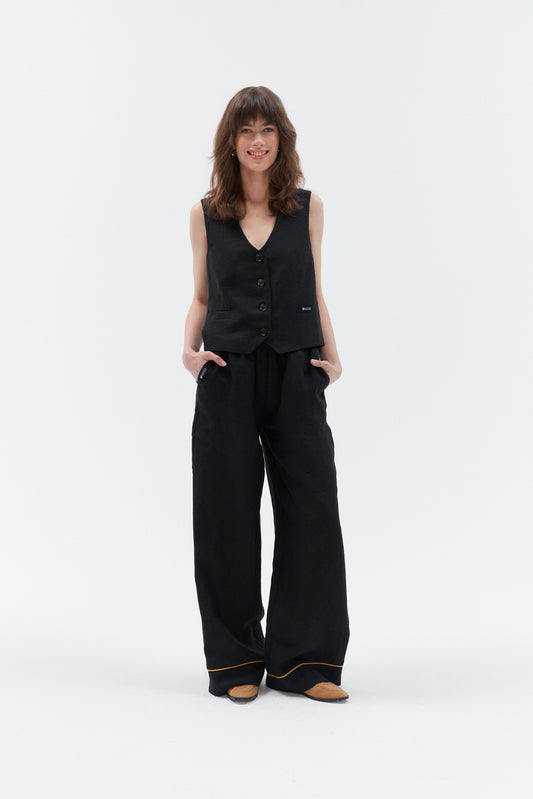 Women's linen pants Impresionante in black with a fitted vest and stylish shoes, showcasing relaxed summer style.
