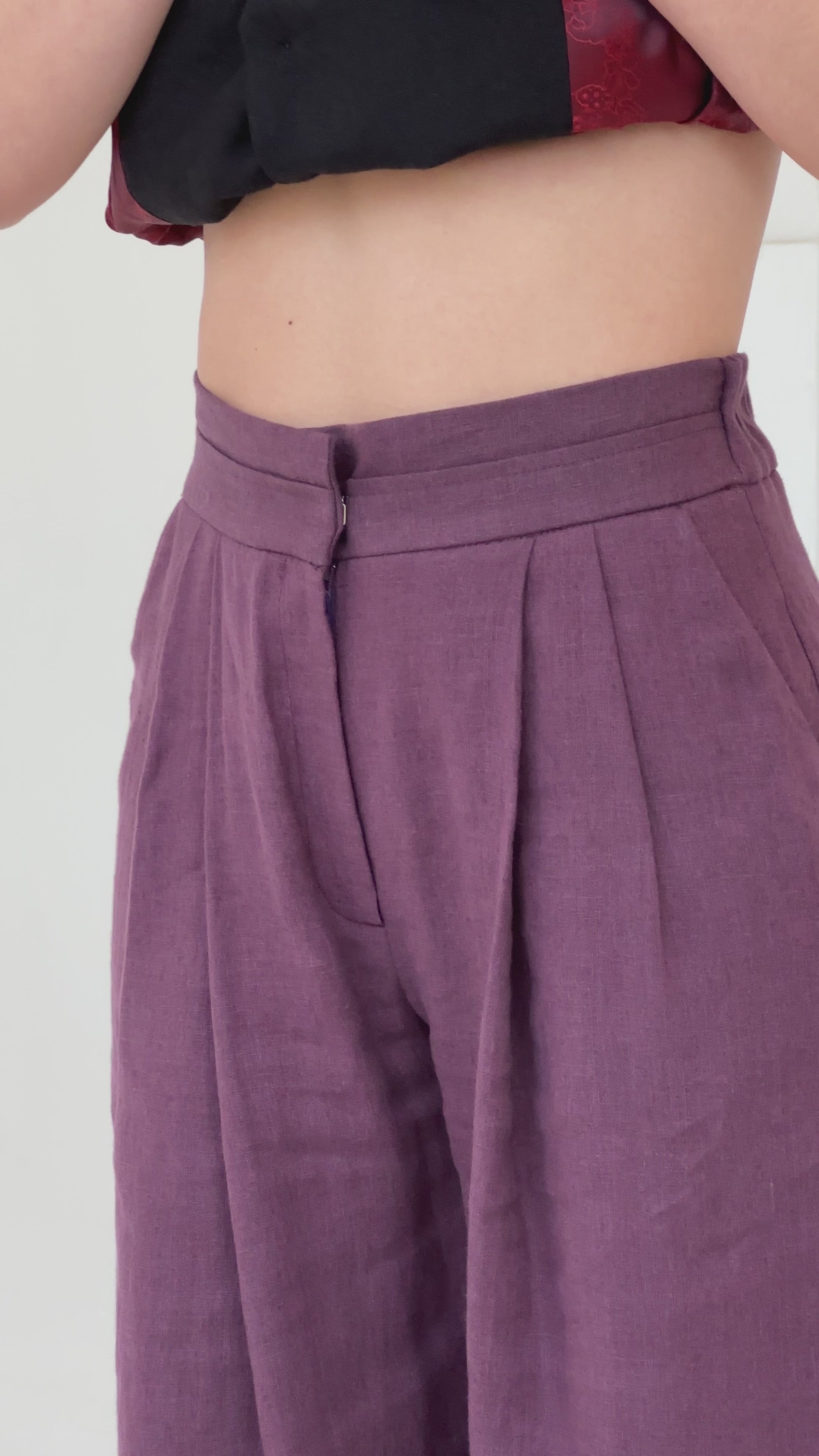 Close-up video of a woman wearing plum-colored high-waisted linen pants, highlighting the elasticated waistband for comfort and the front zipper for a refined, structured look.